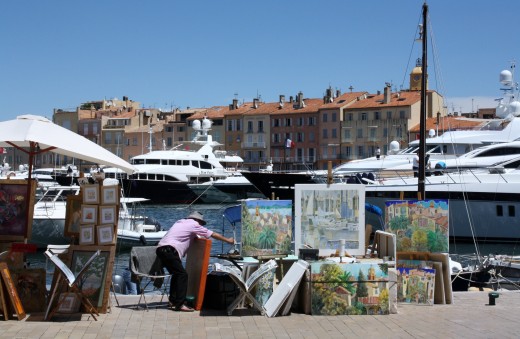 The restaurants of the Quay Juarez is beyond the yachts in the port of St. Tropez. Artisits sell their work in the foreground/