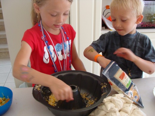 The kids work together to spread the cheese and vegetables along the bottom of the bundt pan.