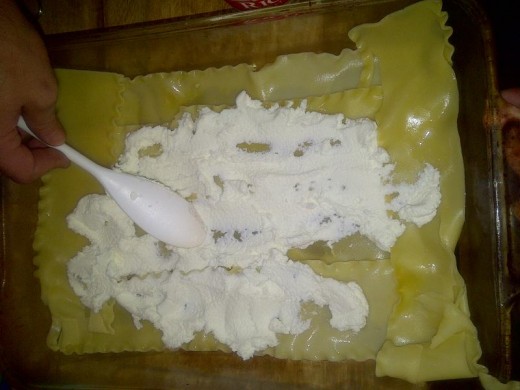 Ricotta cheese being spread onto layer of noodles.