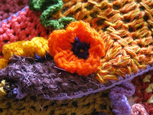 ORANGE CROCHET FLOWER CLOSEUP by Jprescott  DESCRIPTIONCloseup of an orange crocheted flower with a multi-colored crochet fabric background. 