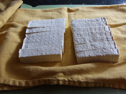 Cutting and lying the tofu out on a towel to absorb the extra liquid. I will lay the rest of the towel over it and then a big book!