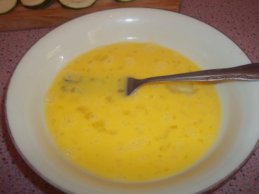 A dredge through beaten eggs helps the flour stick better to the zucchini.