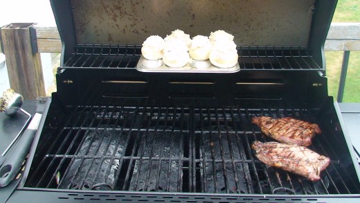 Stuffed mushrooms sitting in a small cup muffin tray on the top rack of the barbecue cooking along with some juicy steak!