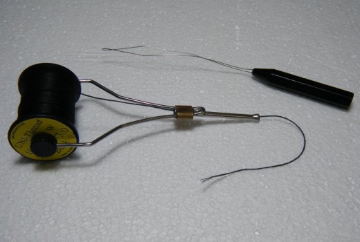 A threaded bobbin (below)  with a bobbin threader (above)