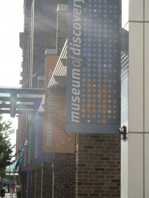 Looking down the sidewalk, the flags decorating the front entrance to the Museum of Discovery 