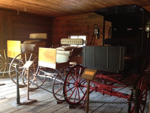 Various carriages now are displayed within the stable. Each is marked with a year and purpose.