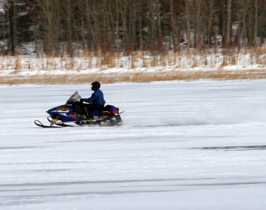 Snowmobile rider driving across a frozen lake.