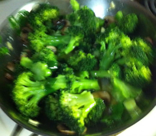 Frying broccoli, green onions, mushrooms, and garlic in olive oil.