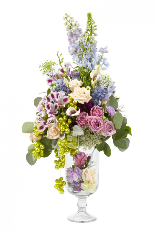 A tall arrangement of lilac blue and white flowers in a glass vase, accented with green beeds