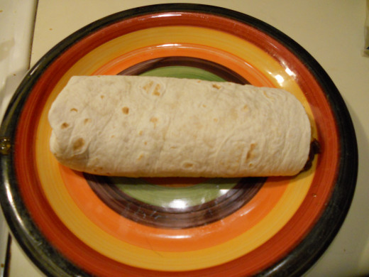 Take the near edge of the tortilla and fold it all the way over the filling.  Use it to pull the filling toward you a bit and then roll the whole burrito over (roll away from you), so the open edge of tortilla is under the burrito.  And voila! 