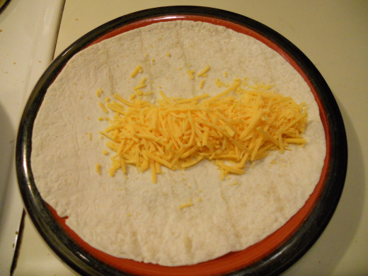 Lay the tortilla out on a plate.  Starting a couple inches in from the edge (in this pic, it's the left edge), sprinkle a line of cheese down the center of the tortilla, all the way to the opposite edge.