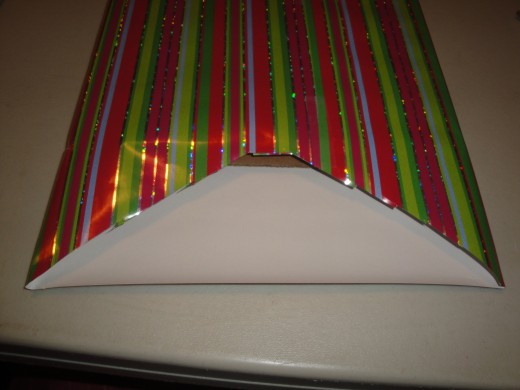 With package up side down, cut a triangle through back side of wrapping paper.  You can place tape at top of triangle to hold paper in place.