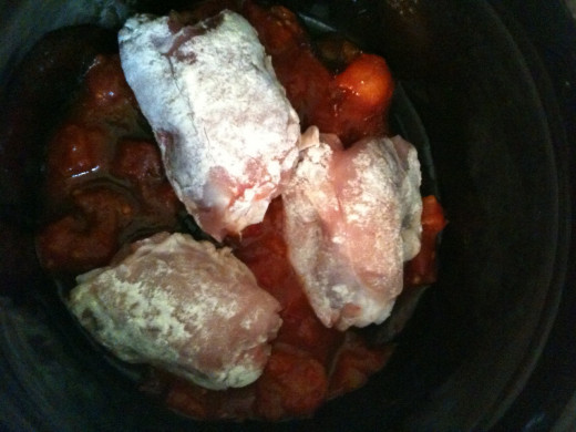 Add half a can of chopped tomatoes to the slow cooker pot and place half the floured chicken thighs on top