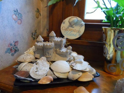 Seashells on a black square ceramic plate. Sand castle on top and Galveston Plaque in the sill.