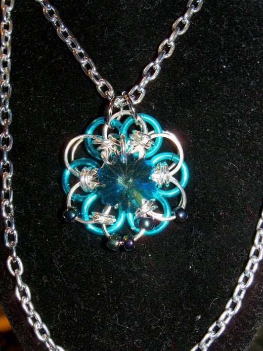 This Japanese 12 in 2 Necklace is made with Light Blue and Silver anodized aluminum rings and has a stainless steel lobster clasp. This hand woven pendant with basic silver chain is approximately 18 inches long. 