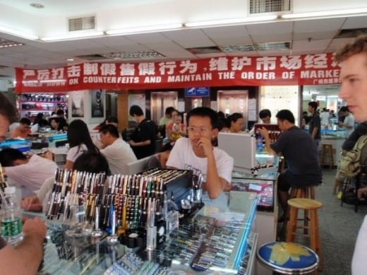 The sign behind reads: 'CRACK DOWN ON COUNTERFEITS AND MAINTAIN THE ORDER OF MARKET ECONOMY' The market economy is a system after all, and systems need to be respected here. Mont blanc pen, anyone? :o)