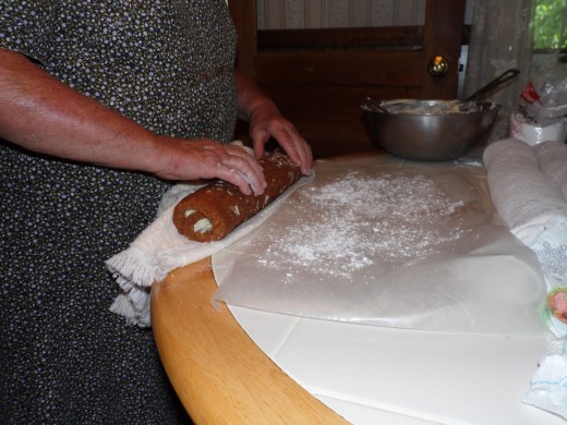 Rolling the pumpkin roll onto a powdered sugar coated piece of wax paper for storage and to chill