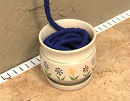 Storage Option for your XHose blue pocket hose coiled inside a small flower pot with painted flowers on the outside