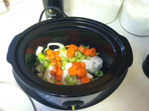 Chopped veggies line the bottom of the crockpot.