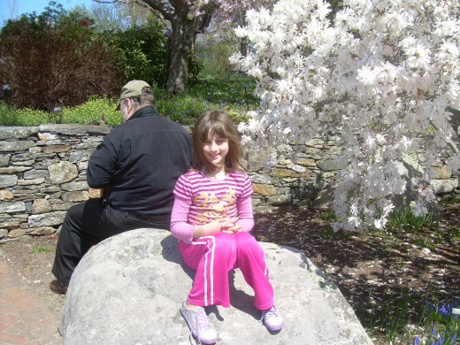 My husband and daughter resting together on a rock by a magnolia tree at Tower Hill Botanical Garden