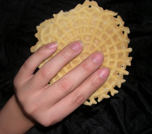 This is a picture of a Anise pizzelle that is in the person hand ready to enjoy. They really look like they will enjoy this Anise pizzelle.