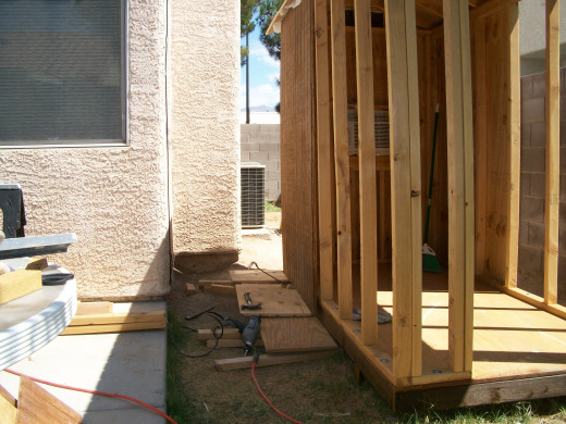 First piece of siding on the other side wall.  Notice the pry bar inserted under the siding so that the siding can be lifted up to touch the roof  using a foot while the hands are used to drill in a screw.