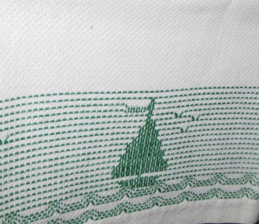 Stitch work depicting a sailboat on vintage kitchen towel.