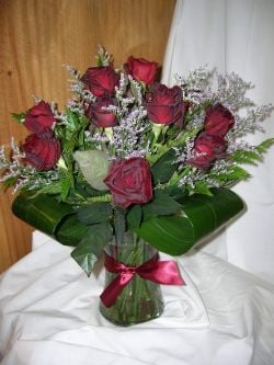 A hand-tied dozen red roses with limonium and premium foliage including aspidistra leaves in a glass vase