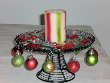 Black wire cake stand with ornaments hung around the edges, candy surrounds a candle in the middle.