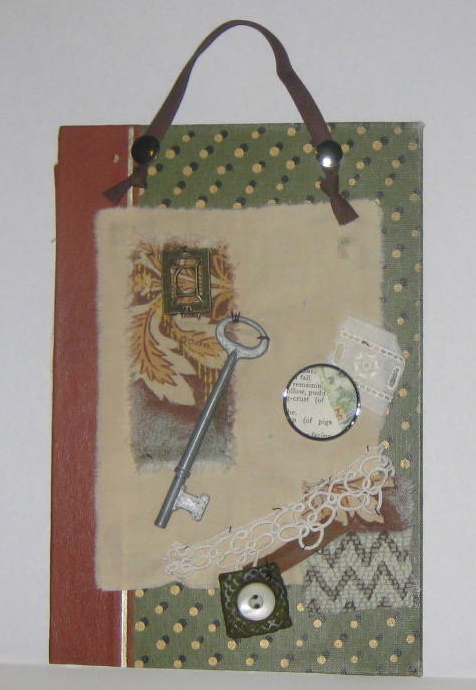 Mixed media collage using a book cover for the base and found objects like fabric, lace, skeleton key, and polymer clay/vintage button tile.